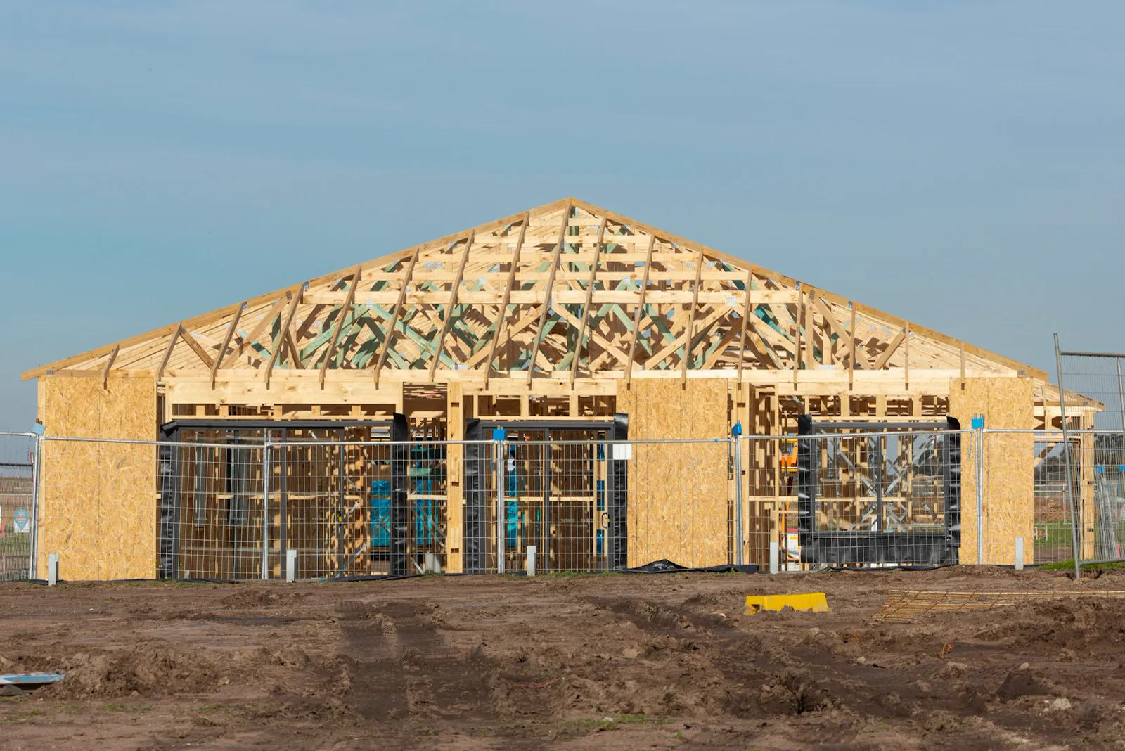 A new home under construction with its roof framing exposed against a blue sky